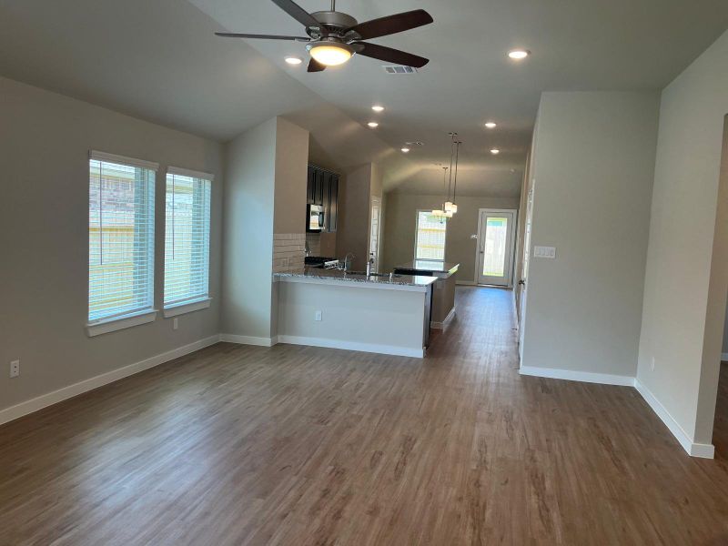 An open living area with wood floors, modern lighting, and large windows next to a sleek kitchen featuring granite countertops.
