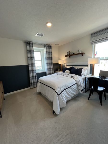 A cozy bedroom with an elegant bed, plaid drapes, and soft carpeting. Features modern decor and ample natural light.