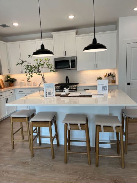 A modern kitchen features sleek white cabinets, pendant lighting, and a spacious island with wooden stools.