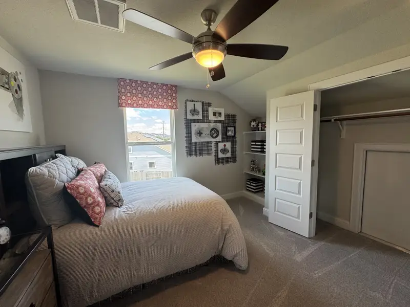 A cozy bedroom featuring soft neutral tones, a ceiling fan, ample closet space, and a large window for natural light.