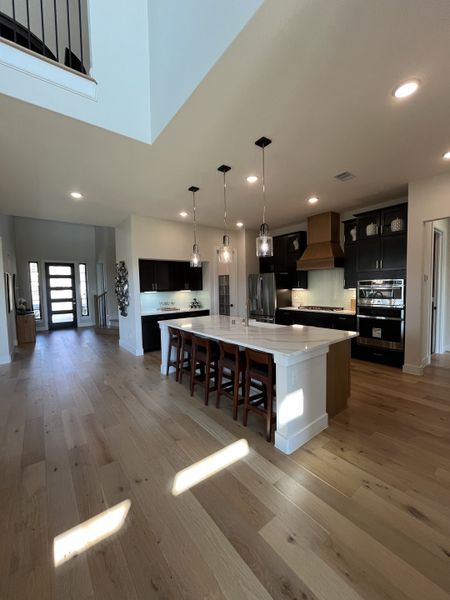 An elegant kitchen with a large island, pendant lighting, wood floors, and modern appliances.