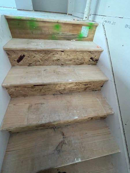 Wooden staircase under construction, with unfinished steps and risers, in a home interior.