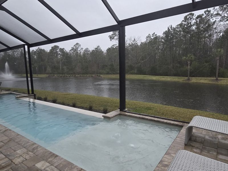 A serene pool area with screened enclosure overlooking a tranquil lake and lush greenery, perfect for relaxation.