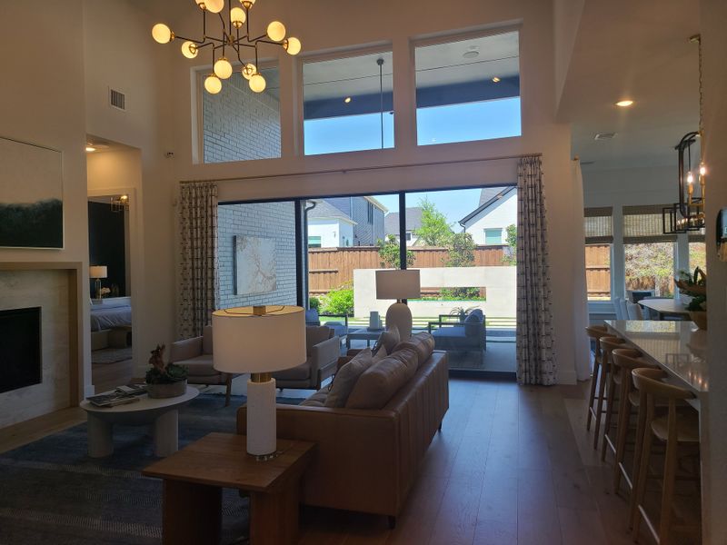 A spacious living room with large windows, modern chandelier, leather sofa, and a view of the patio and garden outside.