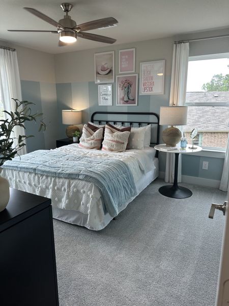 A cozy bedroom featuring modern art, a sleek ceiling fan, and soft textiles with ample natural light.