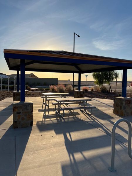 A beautiful park pavilion with picnic tables in Copper Falls by D.R. Horton, Buckeye, AZ, illuminated by the setting sun.