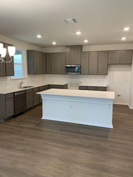 Modern kitchen with gray cabinets, white island, and wood flooring. Bright with recessed lighting and a sleek microwave.
