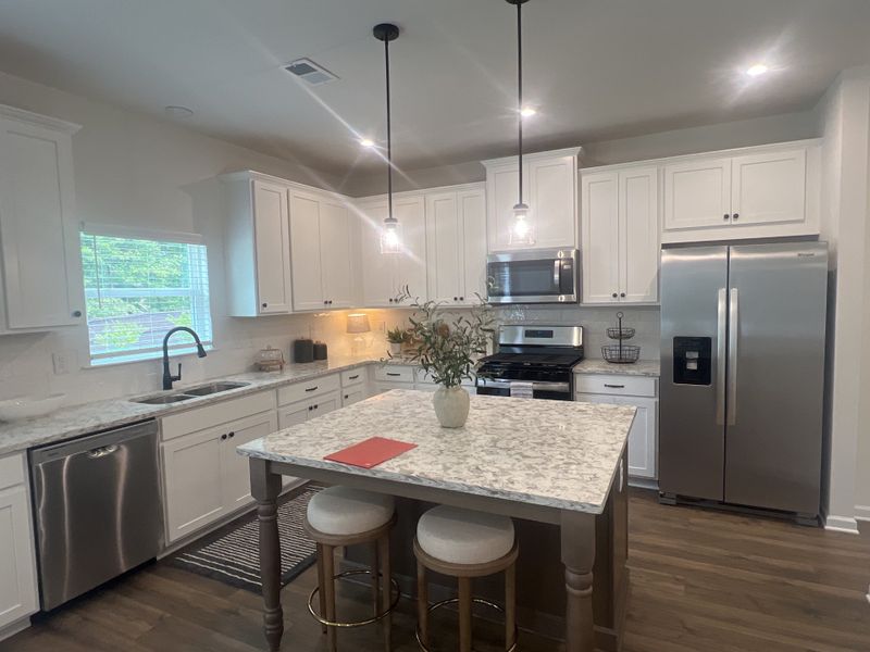 A modern kitchen with white cabinets, marble countertops, stainless steel appliances, and pendant lighting above an island. A modern kitchen with white cabinets, marble countertops, stainless steel appliances, and pendant lighting above an island.