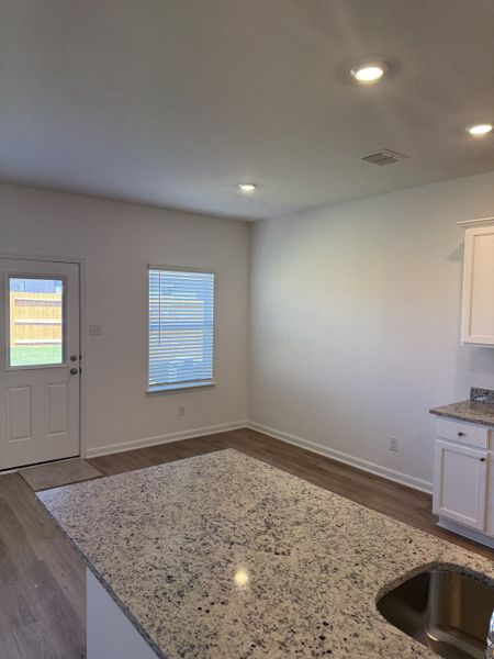 Bright kitchen with granite countertops, recessed lighting, and wood flooring, featuring a door to the backyard.