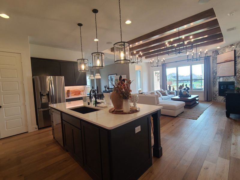An elegant open-concept kitchen with pendant lights, dark cabinetry, and a cozy living area with large windows and chic decor.