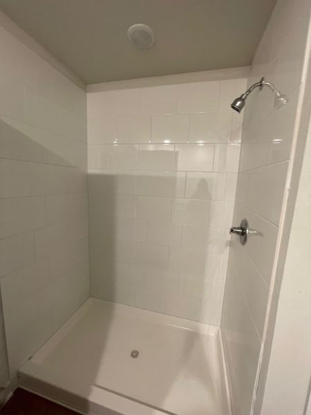 A sleek, minimalist shower with white tiled walls and a modern chrome fixture for a refreshing experience.