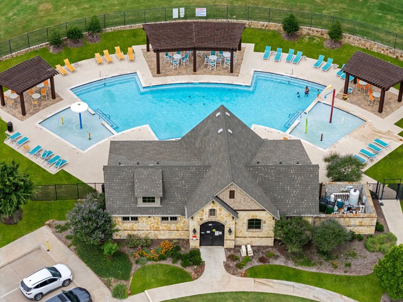 Aerial view of community clubhouse with stone exterior, large pool, splash pad, lounge chairs, and covered pergolas. Aerial view of community clubhouse with stone exterior, large pool, splash pad, lounge chairs, and covered pergolas.