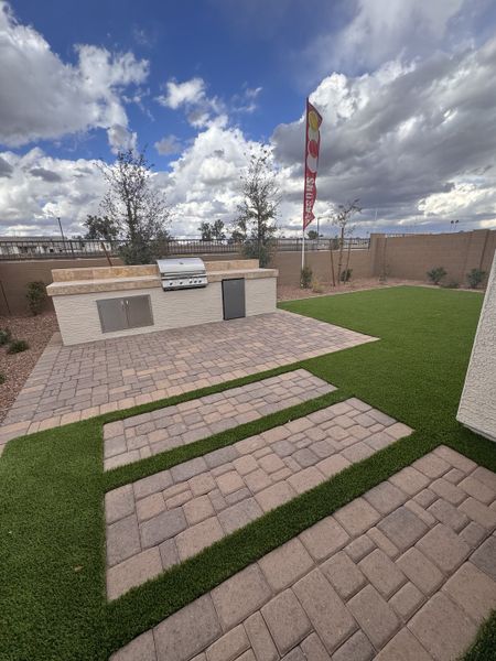 A spacious outdoor area with a built-in grill and paver patio in Seasons at Trevino by Richmond American Homes (Glendale, AZ).