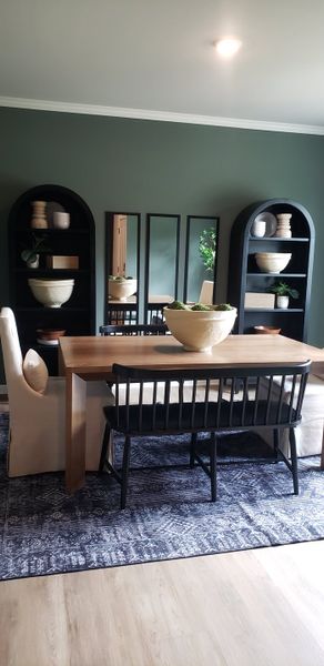A chic dining area with a wooden table, elegant chairs, dark shelves, and stylish decor, set against a rich green wall.