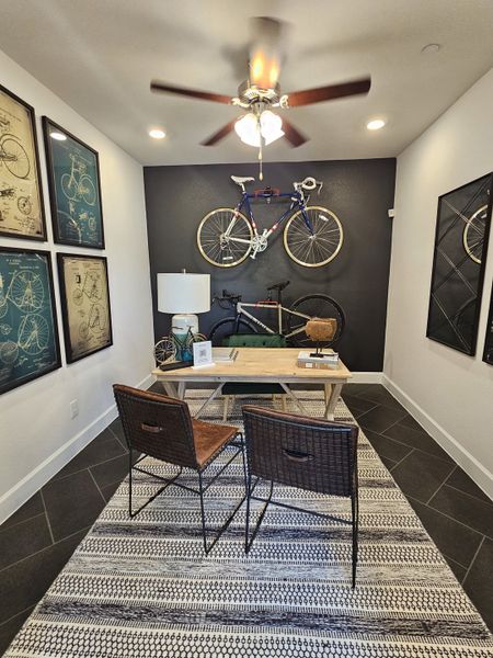 A stylish office with bike decor, framed art, a sleek desk, and woven chairs, enhanced by a textured monochrome rug.