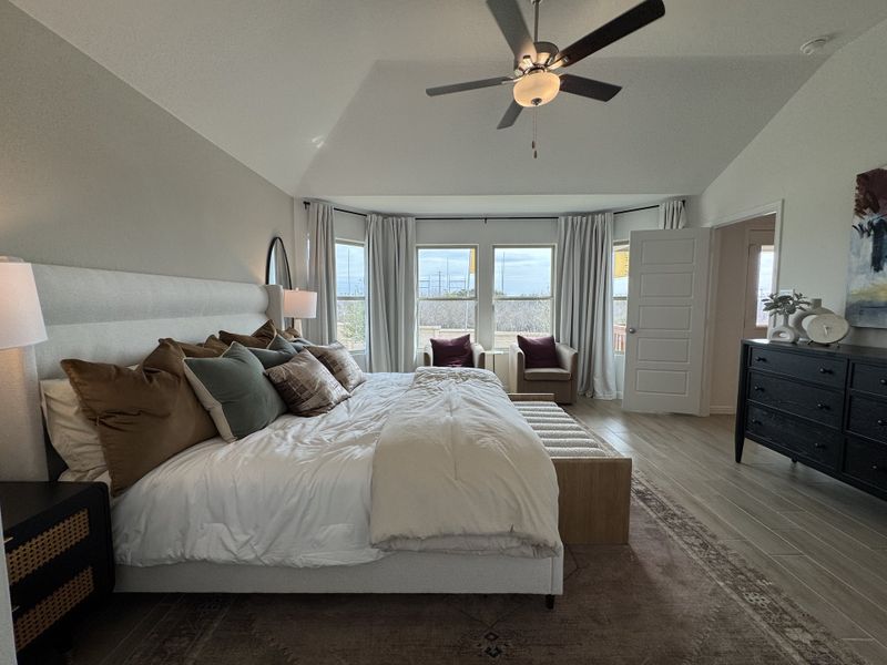 A serene bedroom featuring a plush bed, elegant décor, a ceiling fan, and large windows with natural light.