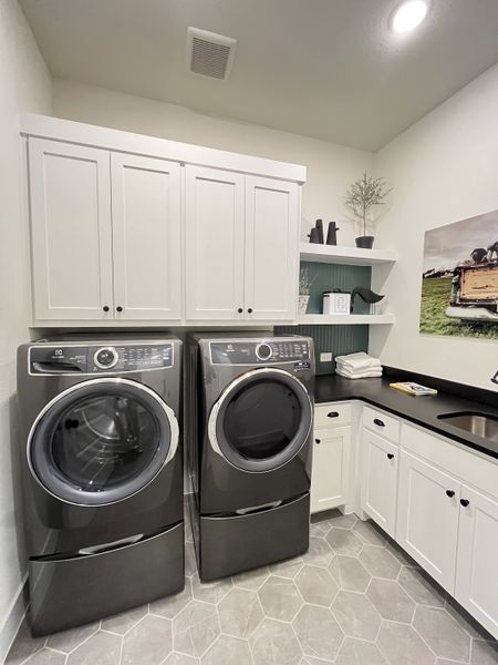 A modern laundry room featuring sleek dark appliances, white cabinetry, and stylish decor accents.