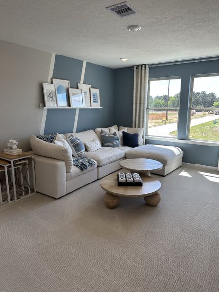 A cozy living room with a plush sectional, geometric accent wall, modern coffee table, and large windows for natural light.
