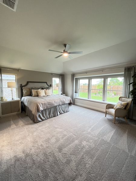 A spacious bedroom with a large bed, modern ceiling fan, and abundant natural light from tall windows overlooking a garden.