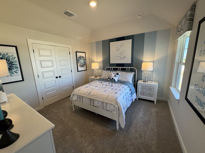 A cozy bedroom with striped walls, elegant artwork, soft carpeting, and a charming bed.