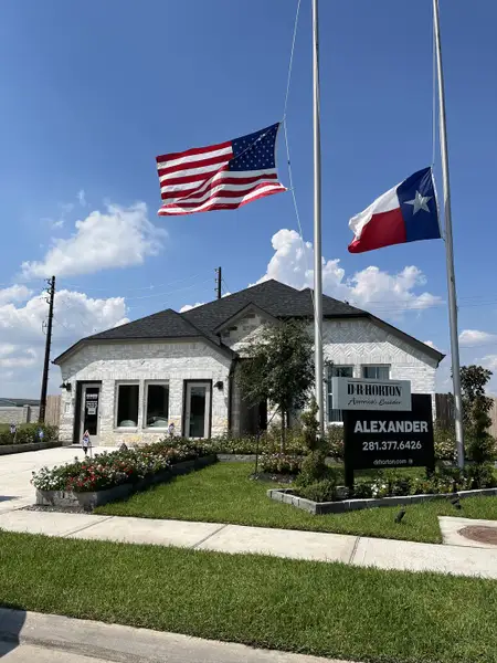 A charming white brick home with flags and lush landscaping in Alexander by D.R. Horton (Pearland, TX).