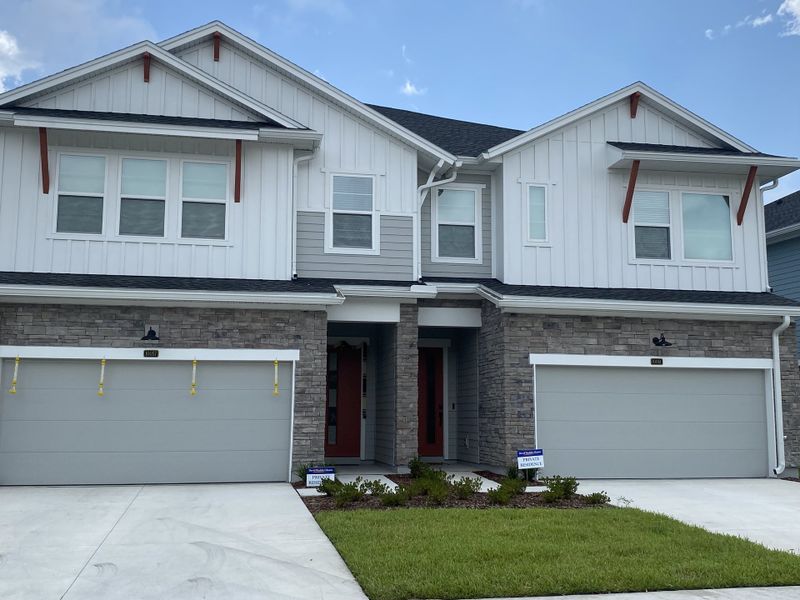 A charming modern duplex with gray stone, white siding, and lush lawn in Kettering at eTown - Paired Villas by David Weekley Homes (Jacksonville, FL).