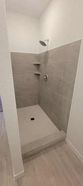 A modern shower with large gray tiles and built-in shelving, offering a sleek and minimalist design.