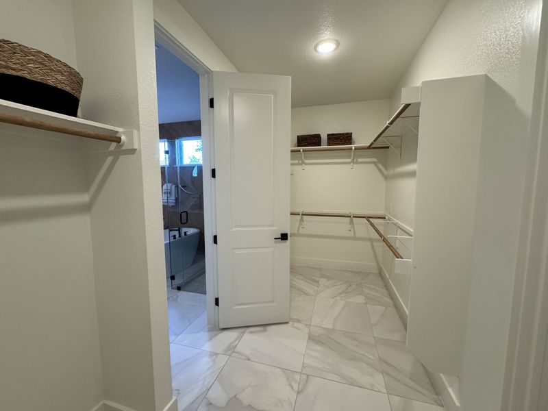 A spacious walk-in closet with elegant marble flooring, ample shelving, and natural light flowing in from an adjacent room.