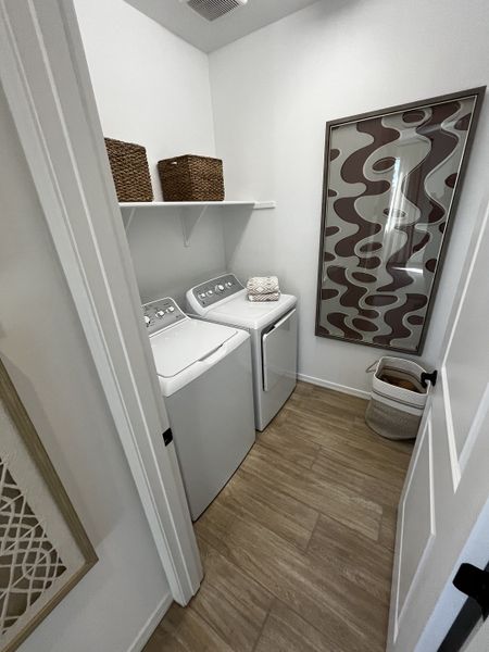 Functional laundry room with wood-look flooring, washer and dryer, woven storage baskets, and modern wall art.