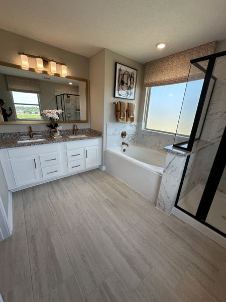 A modern bathroom featuring a double vanity, granite countertops, marble-tiled bathtub, and sleek fixtures.