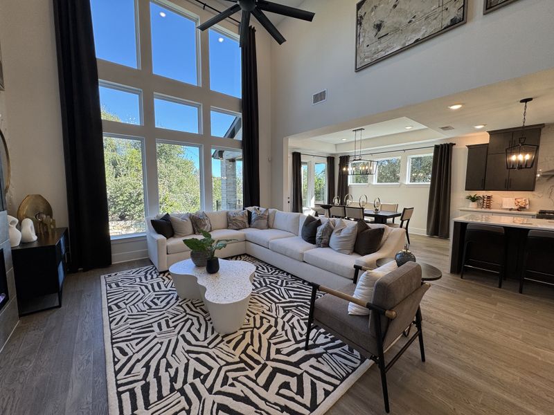 A spacious living area with a high ceiling, large windows, cozy sectional, and modern open-plan kitchen and dining space.