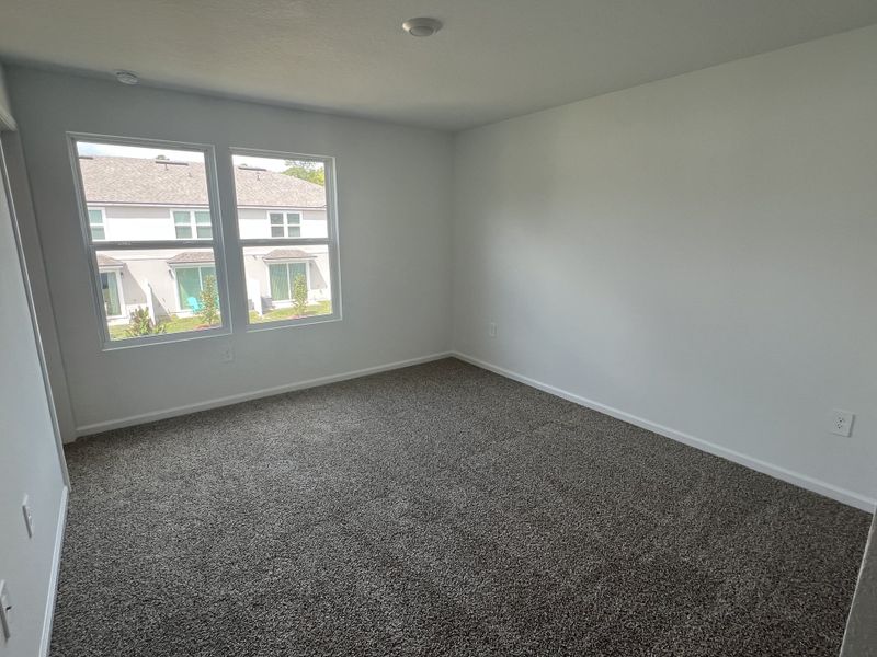 A bright room with plush carpet, neutral walls, and large windows offering a pleasant view of neighboring homes. A bright room with plush carpet, neutral walls, and large windows offering a pleasant view of neighboring homes.