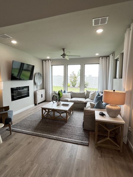 A cozy living area with a plush sectional, large windows, wooden accents, and a wall-mounted TV.