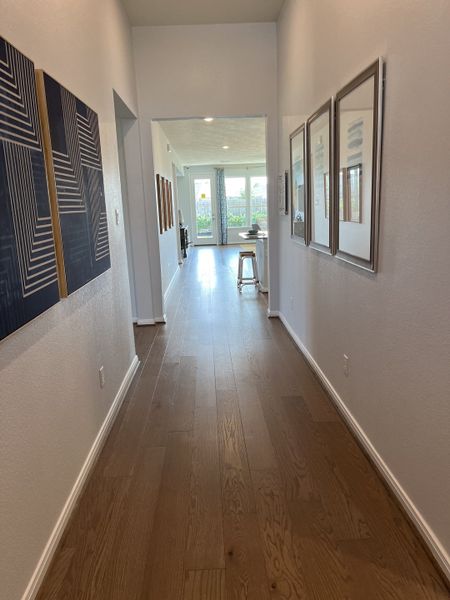 A bright hallway with wood flooring, contemporary wall art, and natural light streaming from a spacious living area.
