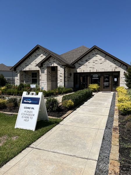 A charming beige brick home with lush landscaping in Massey Oaks - Estate Series by Meritage Homes (Pearland, TX).