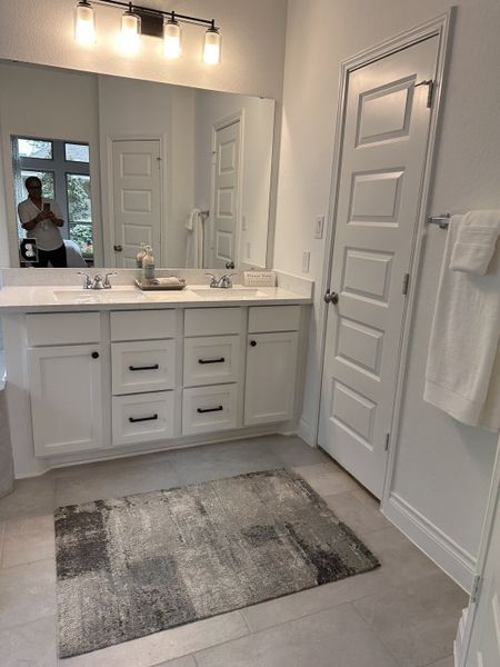 A modern bathroom with a large mirror, double sinks, white cabinetry, and elegant lighting.