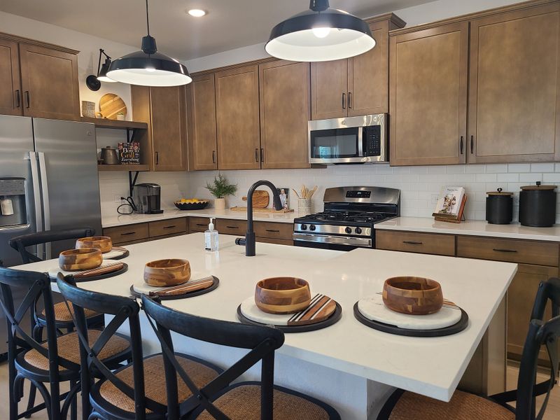 A modern kitchen with wood cabinetry, sleek appliances, and a spacious island with bar seating under stylish pendant lights. A modern kitchen with wood cabinetry, sleek appliances, and a spacious island with bar seating under stylish pendant lights.