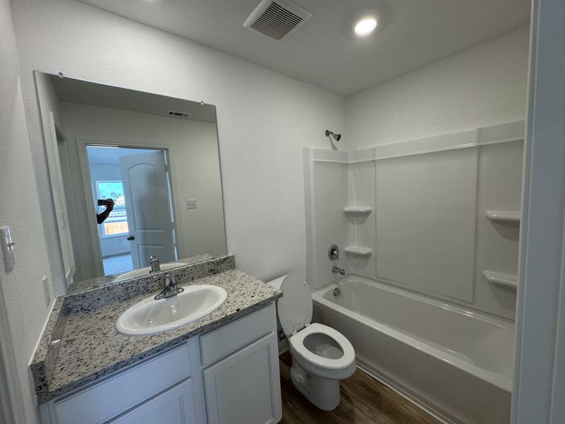 A modern bathroom with a granite-topped vanity, spacious tub, and sleek wood flooring.