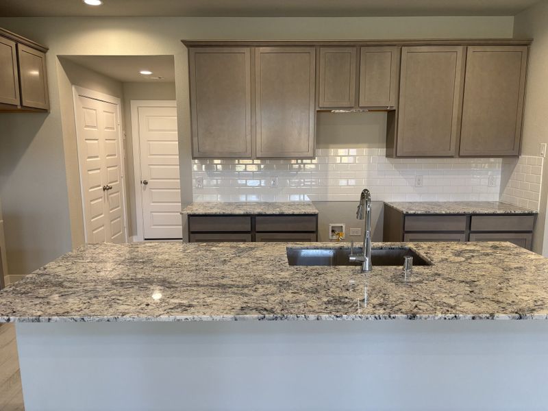 A modern kitchen with granite countertops, white subway tile backsplash, and sleek cabinetry.