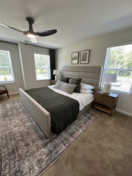 A cozy bedroom featuring a plush bed, plush rug, elegant side tables, and large windows letting in natural light.
