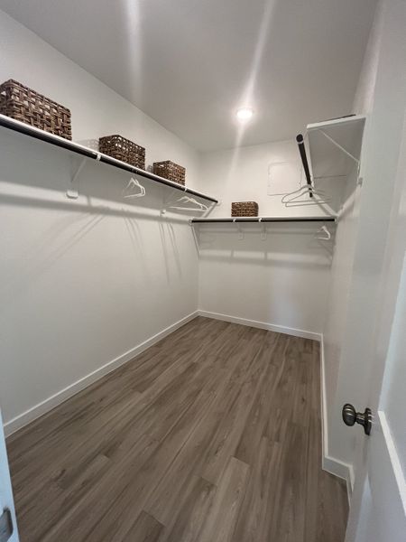 A spacious walk-in closet with wooden flooring, metal hanging rods, and wicker storage baskets. A spacious walk-in closet with wooden flooring, metal hanging rods, and wicker storage baskets.