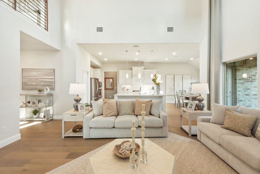 Open-concept living room with two-story ceiling, hardwood floors, and kitchen visible in background