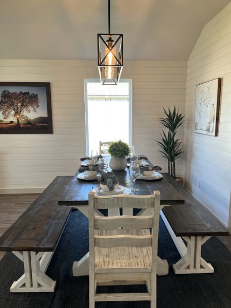 A cozy dining room with a rustic wooden table, benches, vintage lighting, and elegant wall art, creating a welcoming atmosphere.