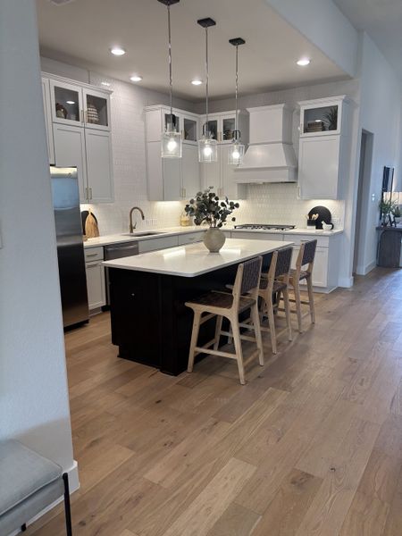 A modern kitchen with sleek white cabinetry, pendant lighting, a center island, and light wood flooring.