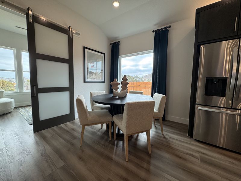 A contemporary dining area with a sleek sliding door, modern table, and cozy chairs, adjacent to a stainless steel fridge.