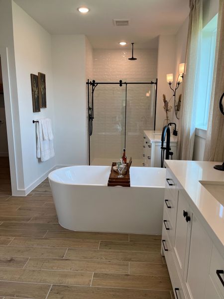 A modern bathroom featuring a freestanding tub, glass shower, wood flooring, and elegant sconces for ambient lighting.
