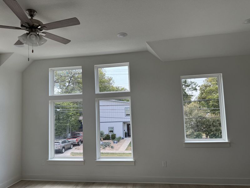 A bright room with large windows, a ceiling fan, and modern design, offering a serene outdoor view.