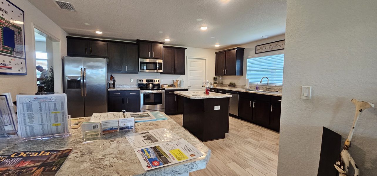 A modern kitchen with dark cabinets, stainless steel appliances, and a marble countertop island.