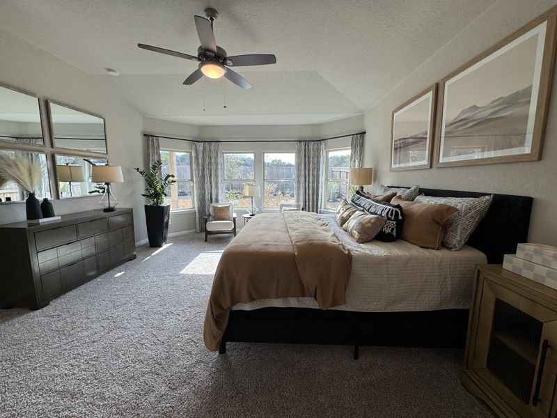 A cozy bedroom with a plush bed, elegant decor, large windows, and a ceiling fan.