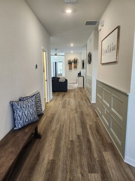 A welcoming hallway with wood flooring, decorative wall paneling, and cozy accents leading to a bright living area.